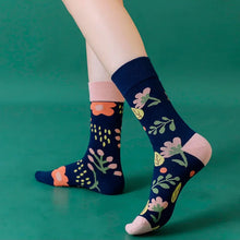 Load image into Gallery viewer, Navy blue socks with floral patterns worn by a person on a green background