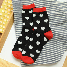 Load image into Gallery viewer, Black socks with white heart patterns and red accents on a striped fabric background