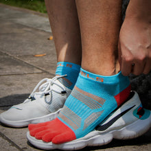 Load image into Gallery viewer, Person wearing white running shoes with blue and red toe socks on a pavement background, emphasizing the elastic cuff design.