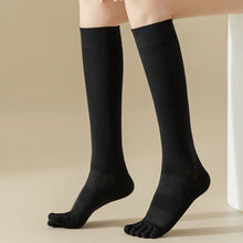 Load image into Gallery viewer, A pair of black knee-high socks with visible toe separation, displayed on a person's leg.