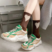 Load image into Gallery viewer, Person wearing brown socks with heart patterns and beige and green sneakers in a minimal indoor setting.