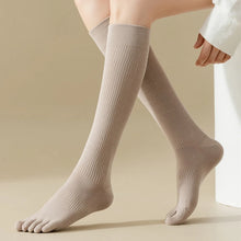Load image into Gallery viewer, A pair of beige knee-high socks with visible toe separation, displayed on a person's leg.