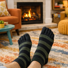 Load image into Gallery viewer, Person wearing striped socks in a cozy living room with a fireplace.
