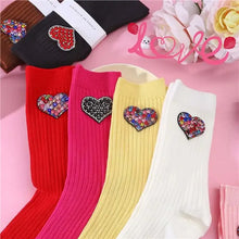 Load image into Gallery viewer, Four colorful socks with heart-shaped embellishments on a pink background.
