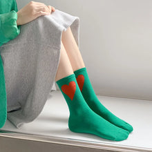 Load image into Gallery viewer, Person wearing green socks with red hearts sitting on a windowsill.
