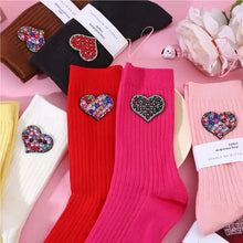 Load image into Gallery viewer, Colorful socks with heart-shaped embellishments on a pink surface with flowers.
