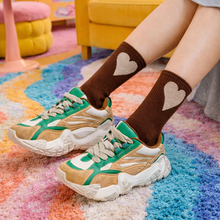 Load image into Gallery viewer, Person wearing brown socks with heart designs in a colorful room.

